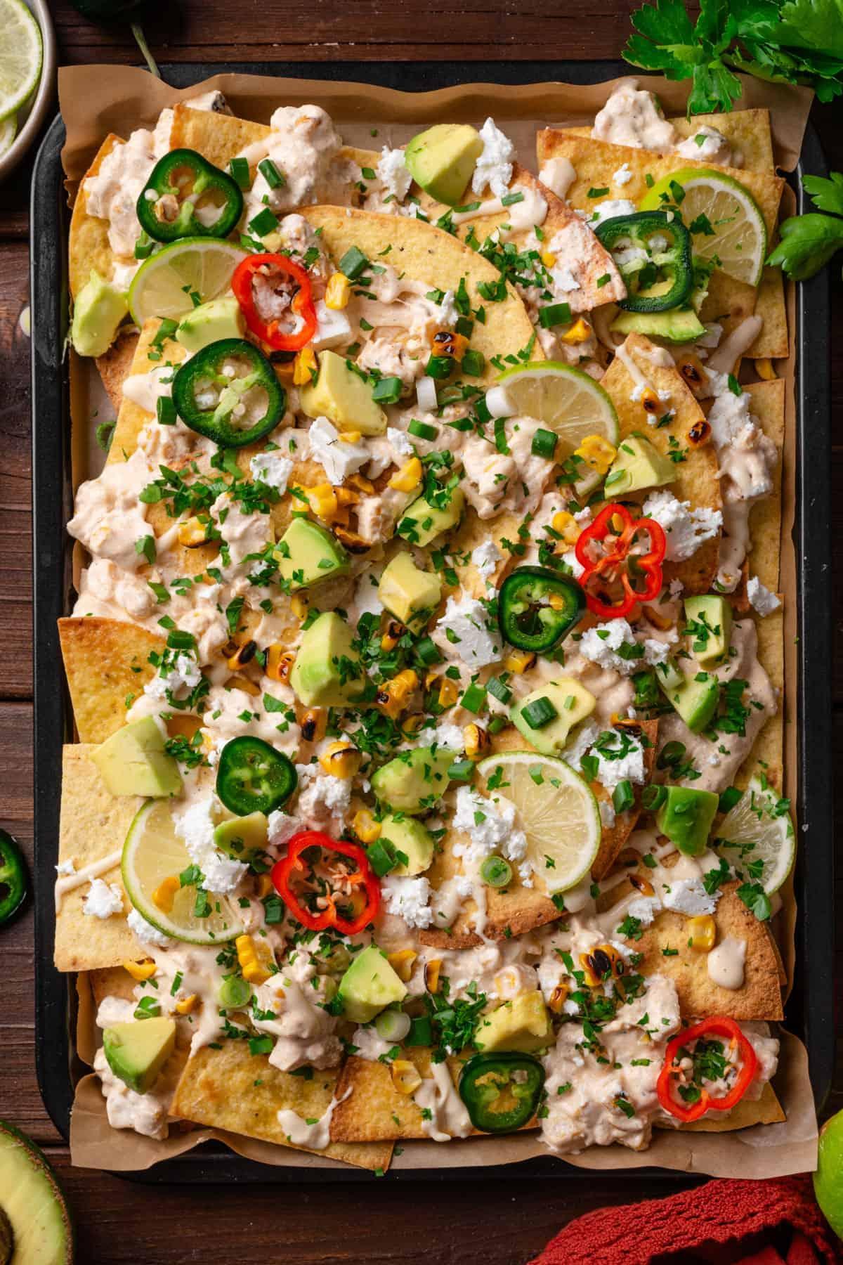 Overhead shot of a baking sheet filled with Street Corn Nachos Supreme, topped with various colorful ingredients