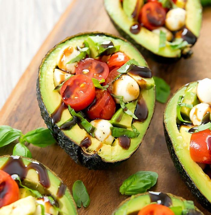Close-up of someone assembling Caprese stuffed avocados at a campsite