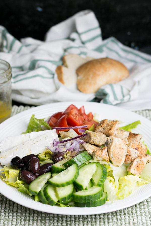 Ingredients for lemon oregano chicken and greek salad laid out on a wooden table