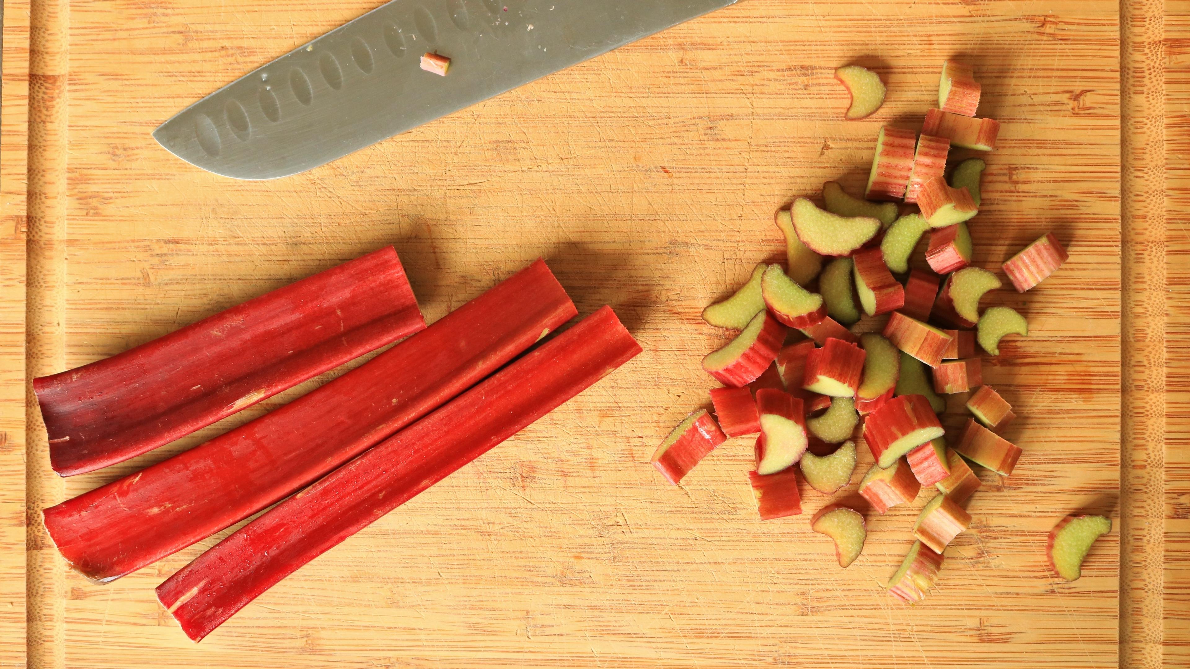 overhead shot of raw rhubarb being chopped on a wooden cutting board