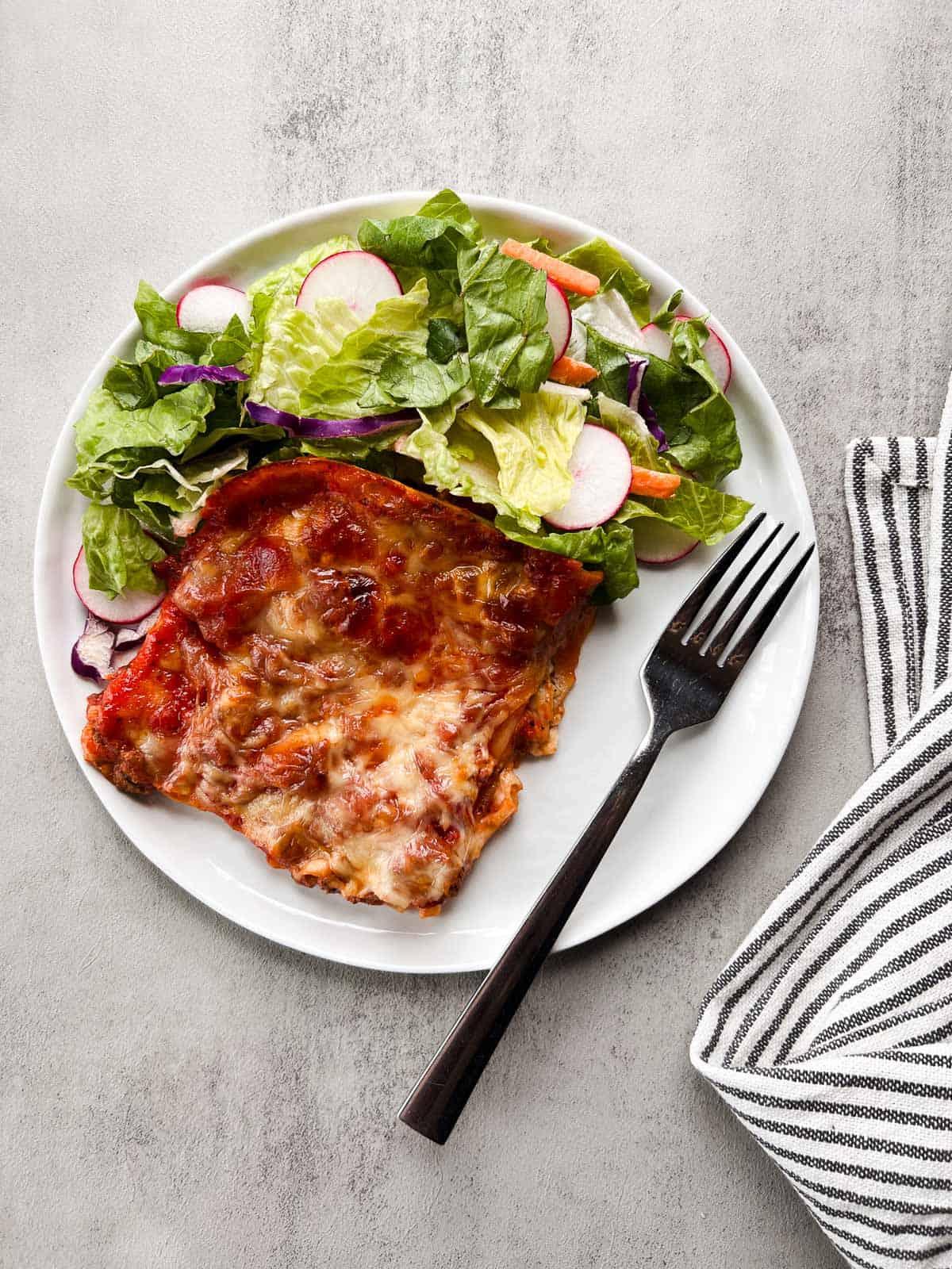 A slice of lasagna being served on a plate, with a side salad