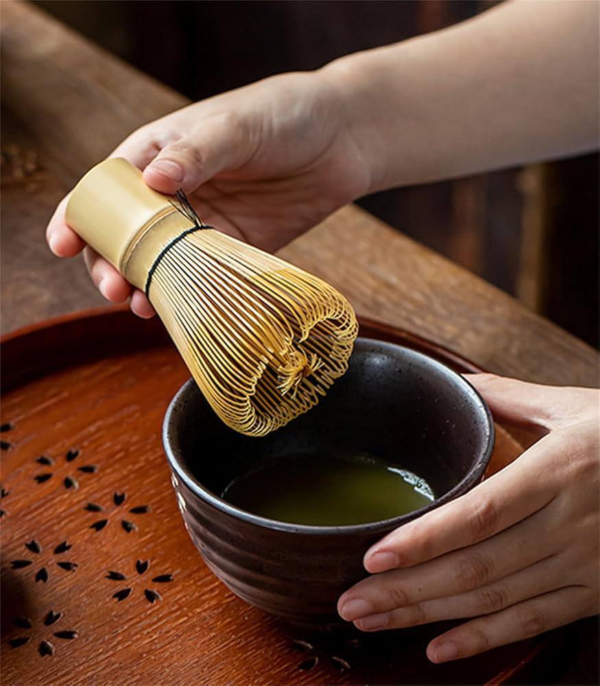 A person preparing matcha tea with a bamboo whisk in a traditional setting