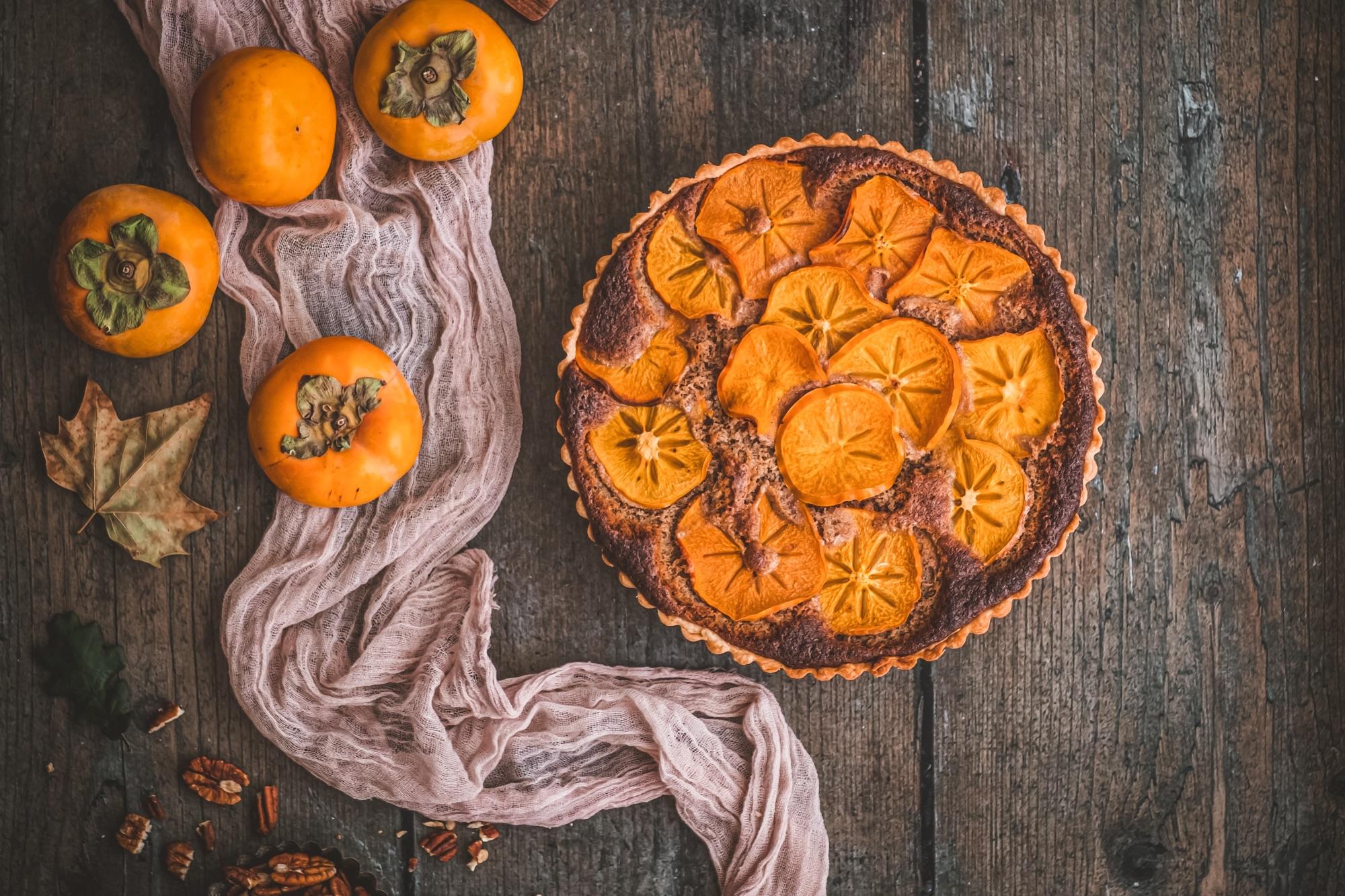 overhead shot of a freshly baked persimmon pecan praline tart on a wooden surface