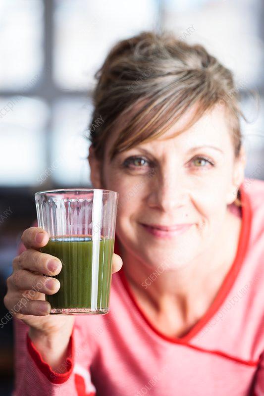 woman smiling while drinking a green smoothie
