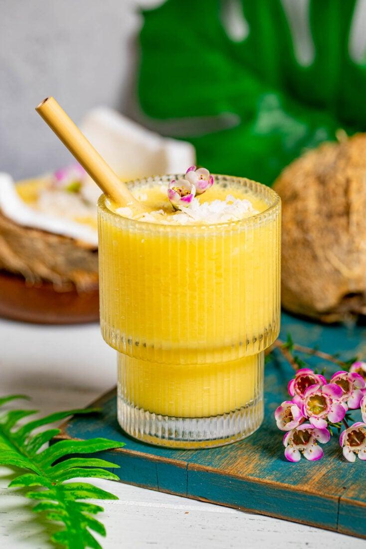 close up shot of a glass filled with a vibrant yellow mango coconut smoothie