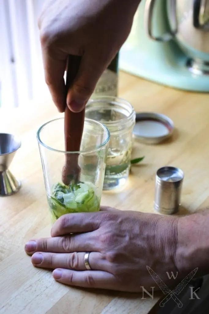 cucumber and mint leaves being muddled in cocktail shaker