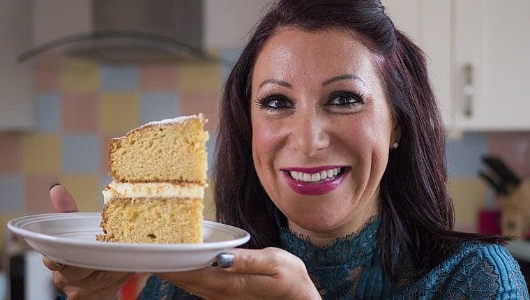 A woman smiling while holding a slice of sponge cake