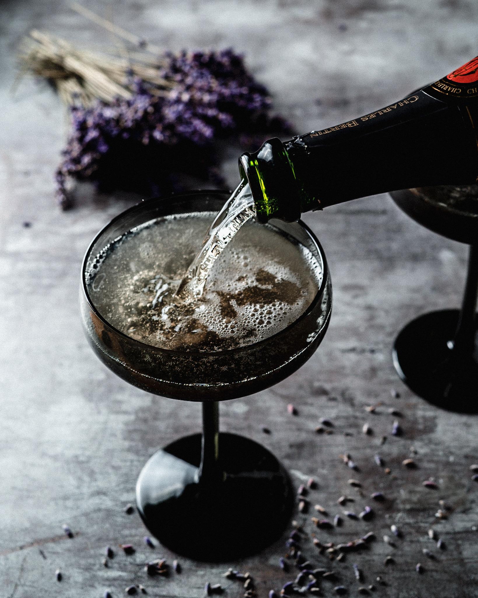 Pouring sparkling wine into a glass filled with ice, elderflower liqueur, and lavender syrup