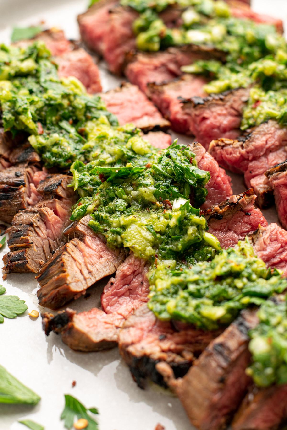 close-up shot of grilled flank steak slices topped with chimichurri sauce