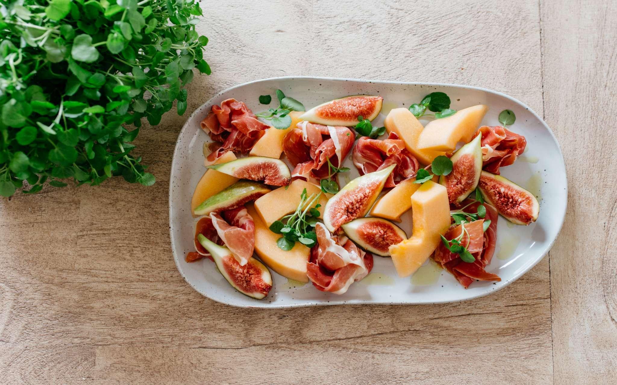 A person serving a Watermelon Prosciutto Fig Salad onto a plate