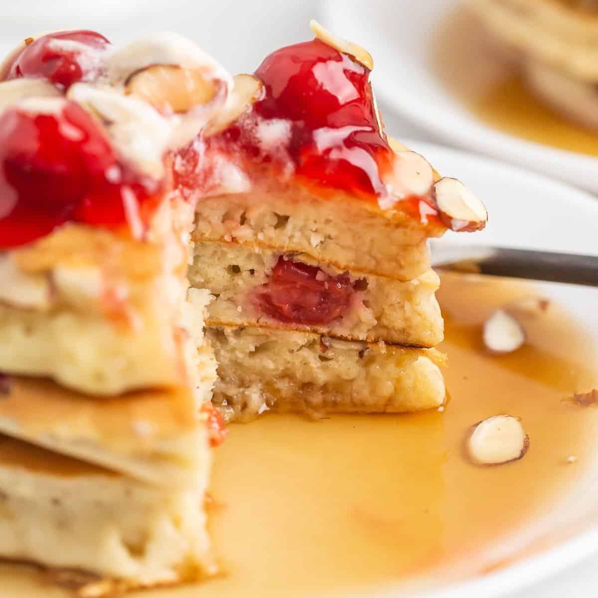 aerial view of a stack of cherry almond protein pancakes with syrup and fresh cherries