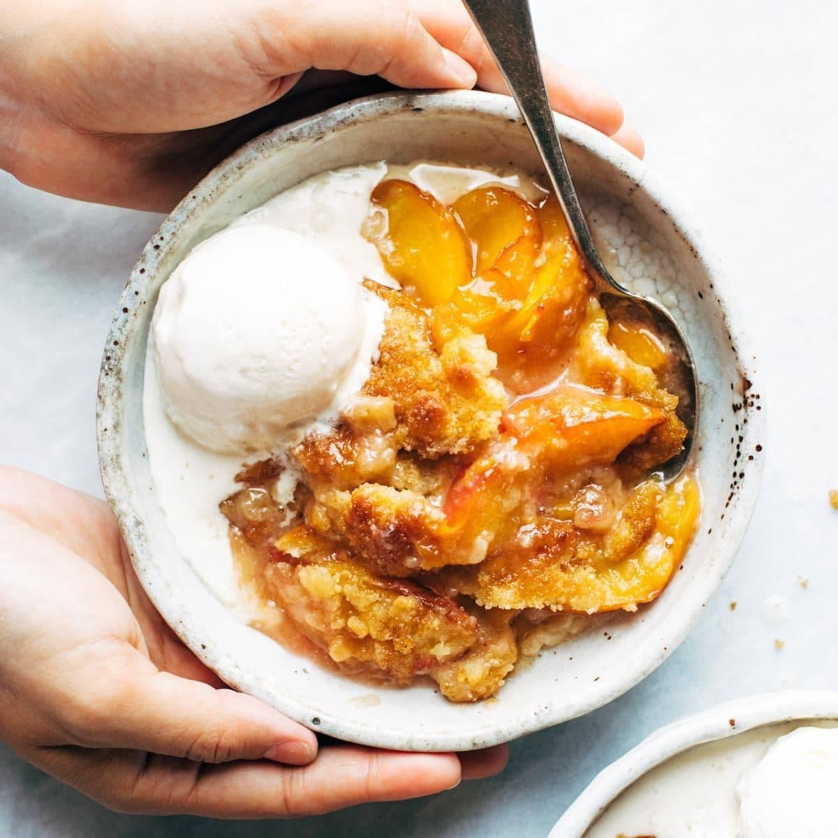 slice of peach cobbler being served with a scoop of vanilla ice cream