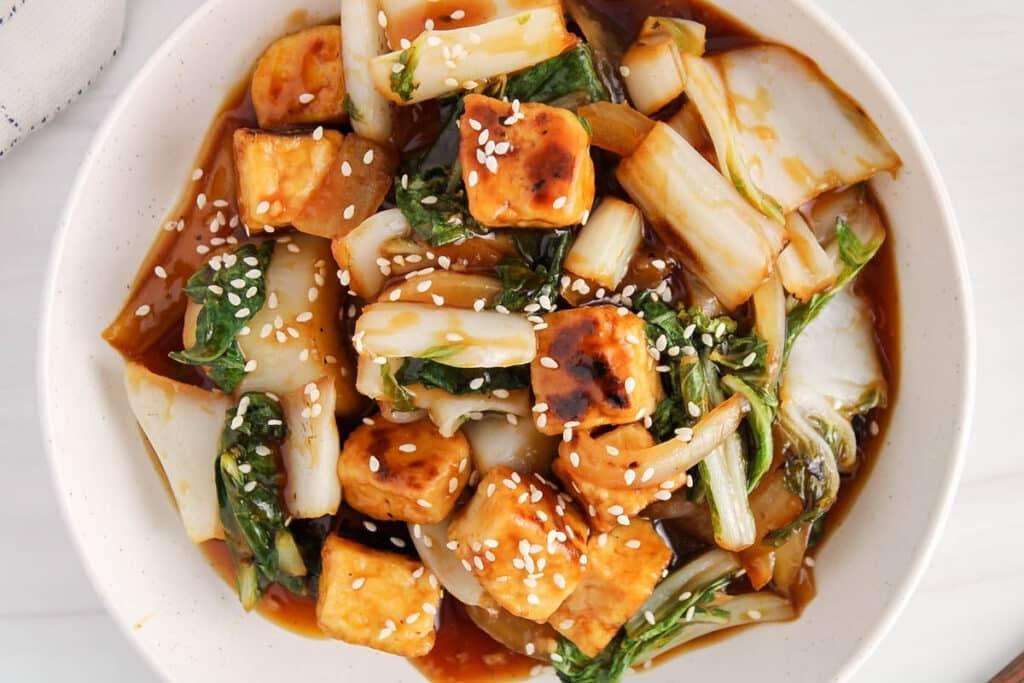 close up shot of tofu and bok choy stir-fry plated and garnished with scallions and sesame seeds