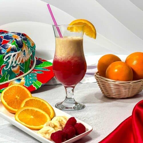 vibrant hurricane protein smoothie in a glass with tropical fruits around it