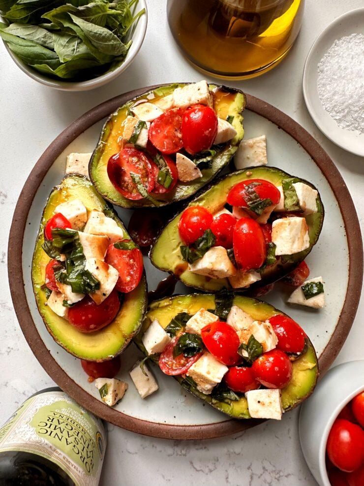 Overhead shot of several Caprese stuffed avocados arranged on a wooden platter at a campsite