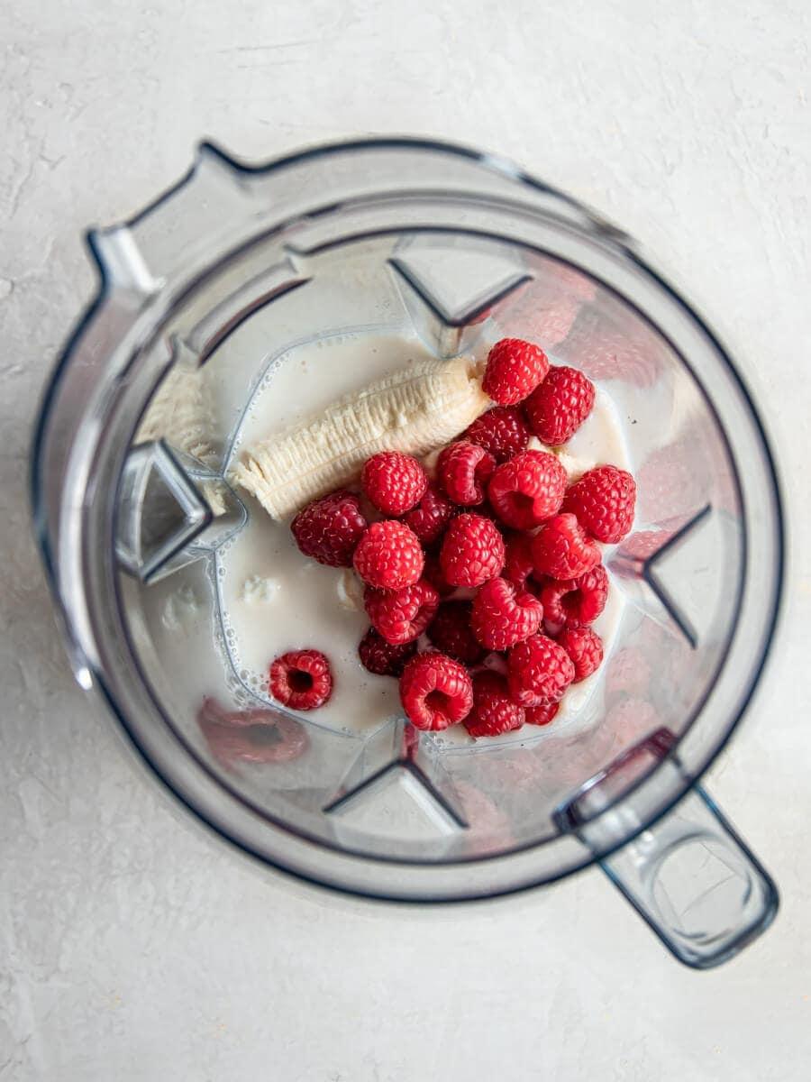 A close-up shot of a blender filled with raspberries, yogurt, and other ingredients.