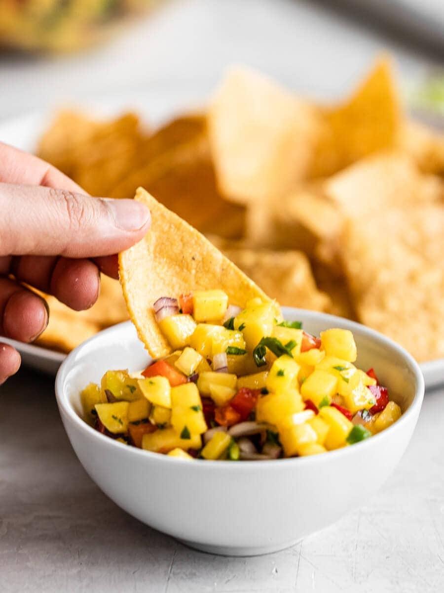 overhead shot of a person scooping coconut lime mango salsa with a tortilla chip