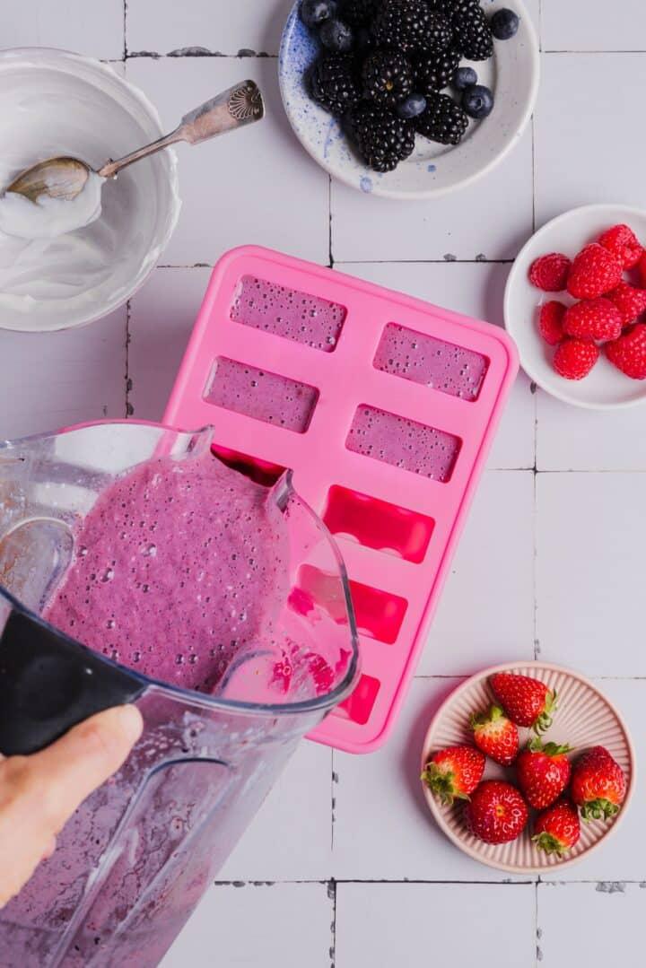 blended black raspberry mixture being poured into popsicle molds