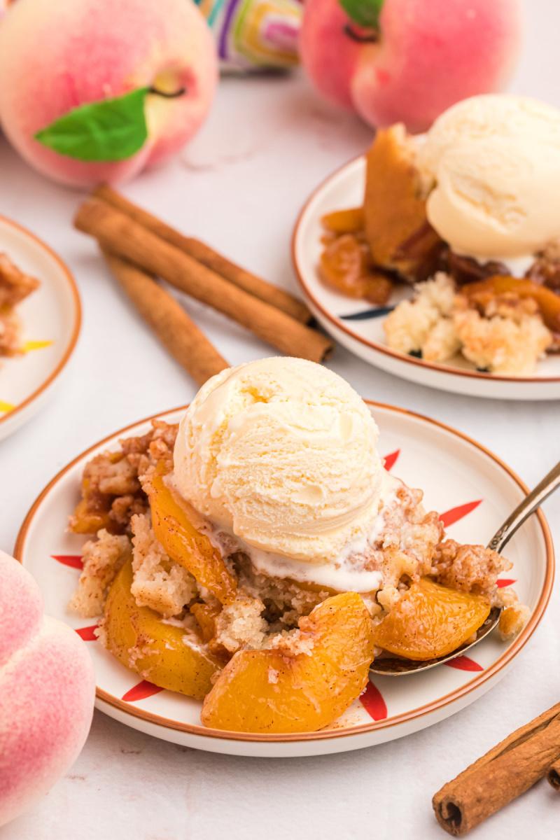 a hand scooping a serving of warm milk chocolate peach cobbler onto a plate