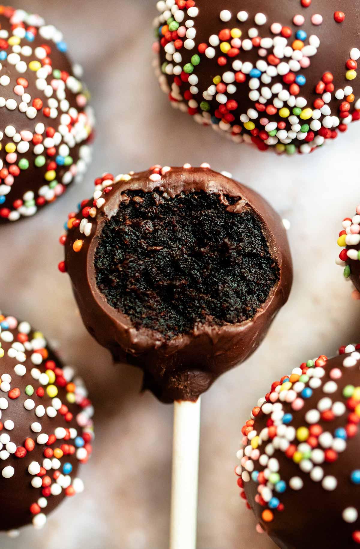 close-up of a hand dipping a mini-cupcake cake pop into melted chocolate