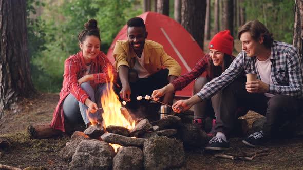 Group of people sitting around a campfire, eating campfire pigs in a blanket