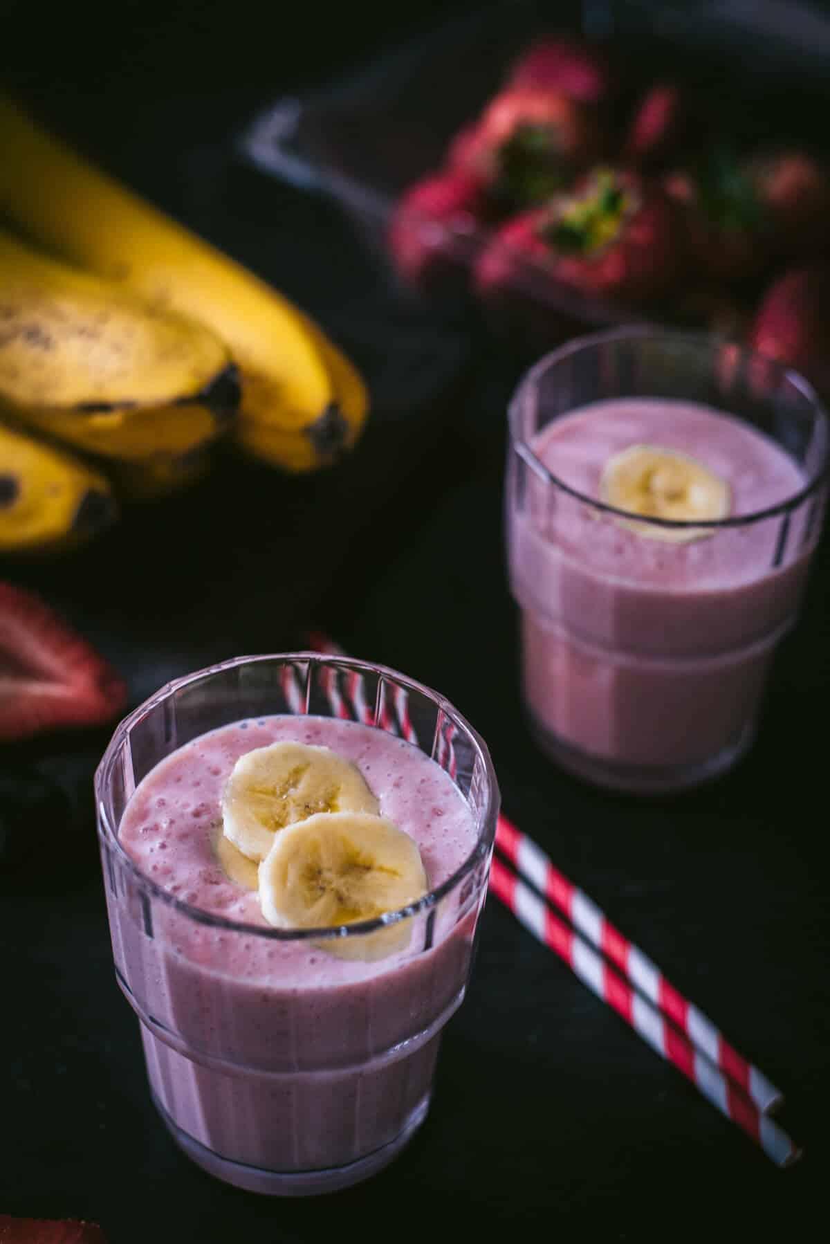 a vibrant strawberry banana protein smoothie in a glass with fresh strawberries and bananas around it