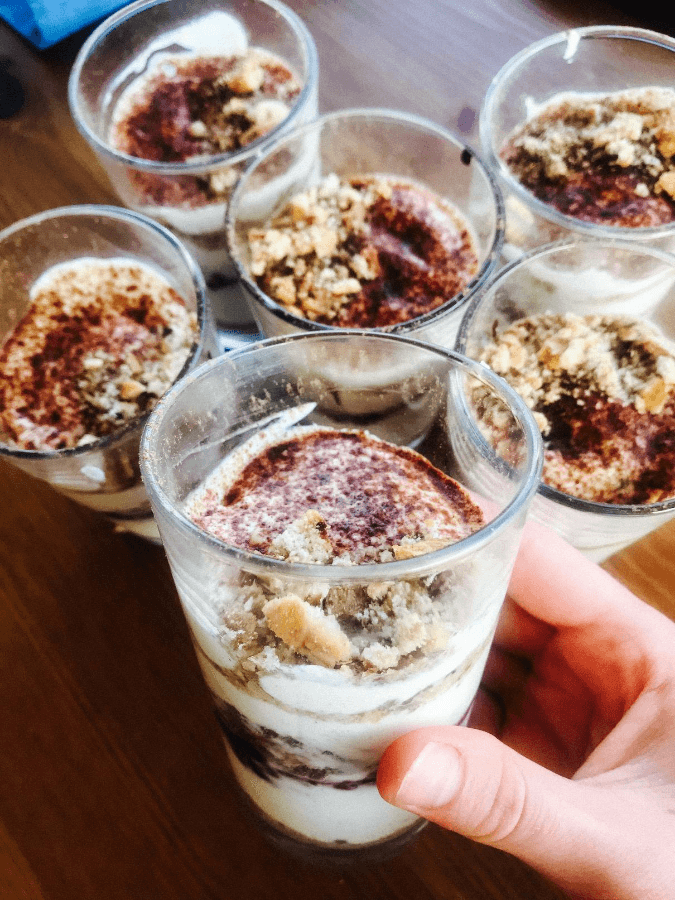 A person layering the Tayberry Tropical Tiramisu Parfait in a glass dish