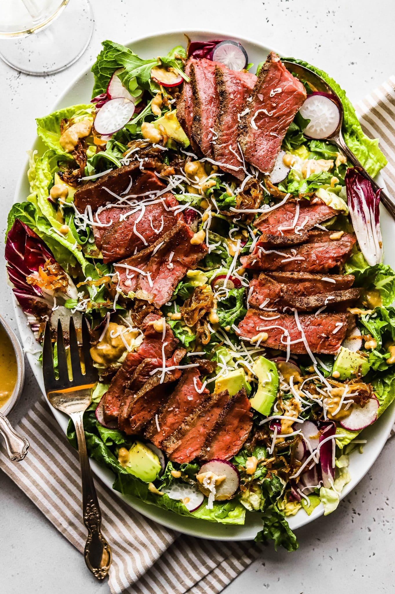 Father's Day steak salad with caramelized onions and goat cheese on a wooden table