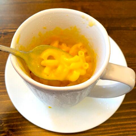 A coffee mug filled with mac and cheese, with a spoon resting inside, ready to be eaten