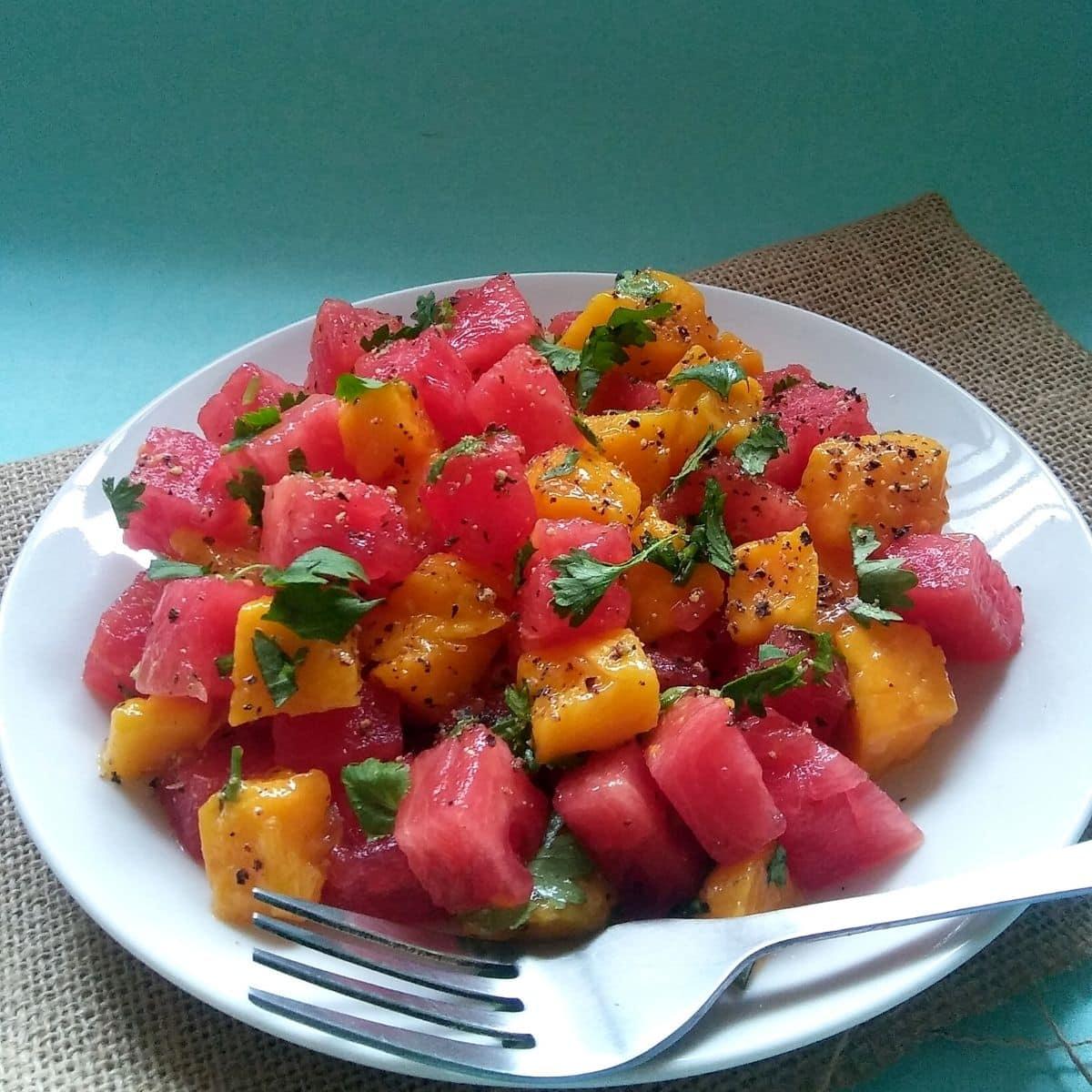 close-up of a spoonful of watermelon mango salad being lifted from a bowl
