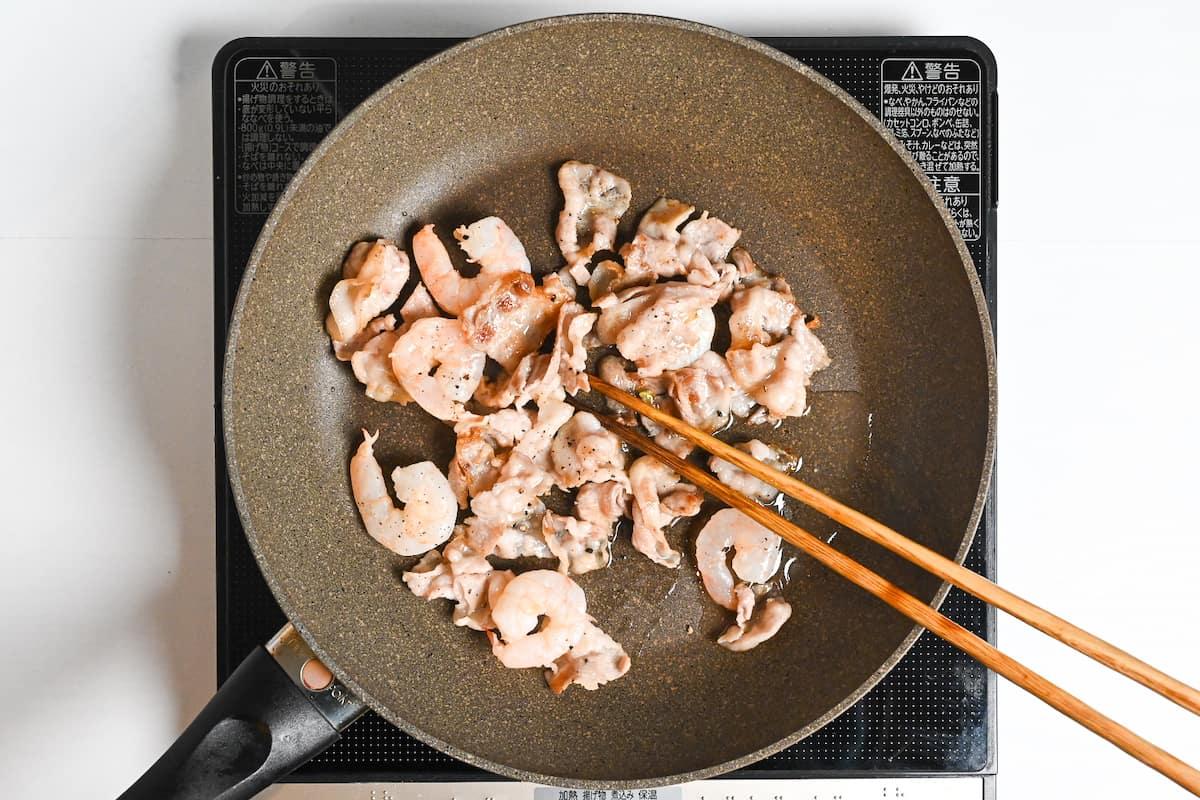 A person preparing the Nagasaki Champon in a home kitchen, stir-frying the ingredients in a wok.