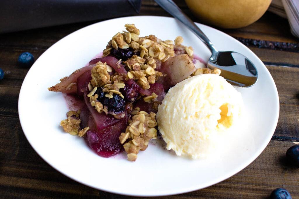a slice of pear and blueberry crisp being served, with the steam rising and a close-up of the golden brown topping