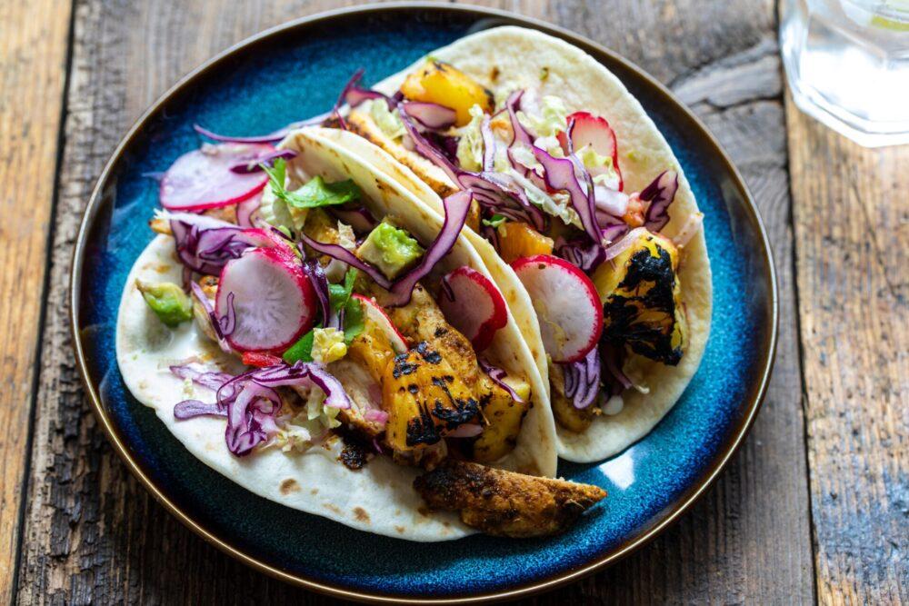 overhead shot of colorful grilled chicken and pineapple tacos with various toppings