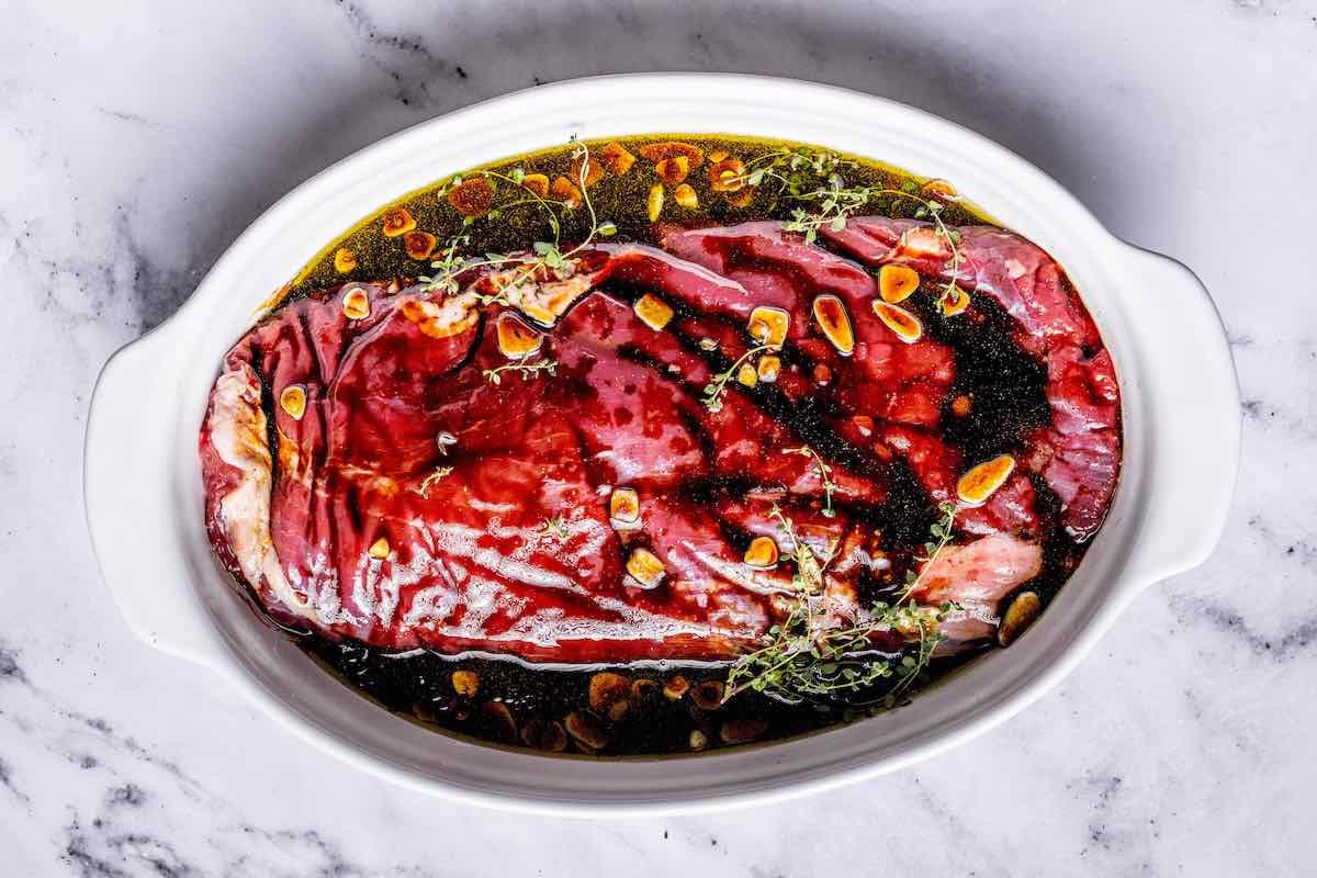 raw flank steak marinating in a bowl