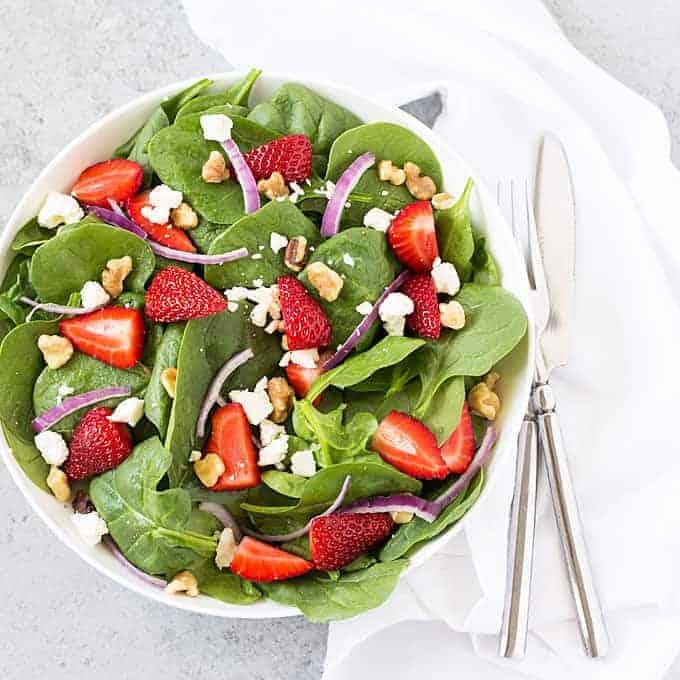 Overhead shot of a colorful strawberry spinach salad in a white bowl