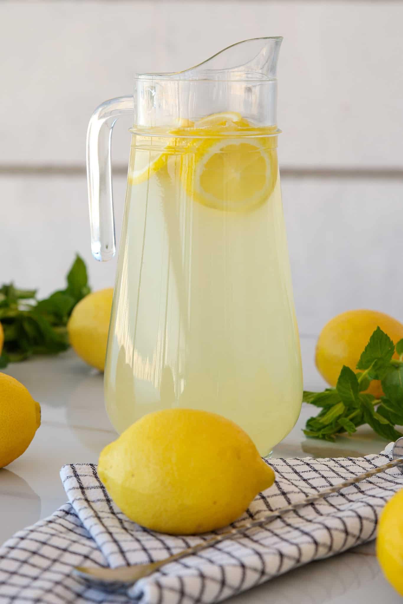 A pitcher of homemade citrus lemonade surrounded by fresh lemons, sugar, and mint sprigs