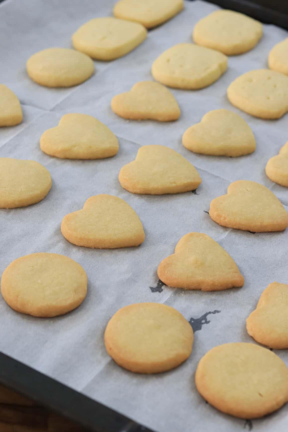 Various unbaked butter cookie shapes on a baking sheet, parchment paper
