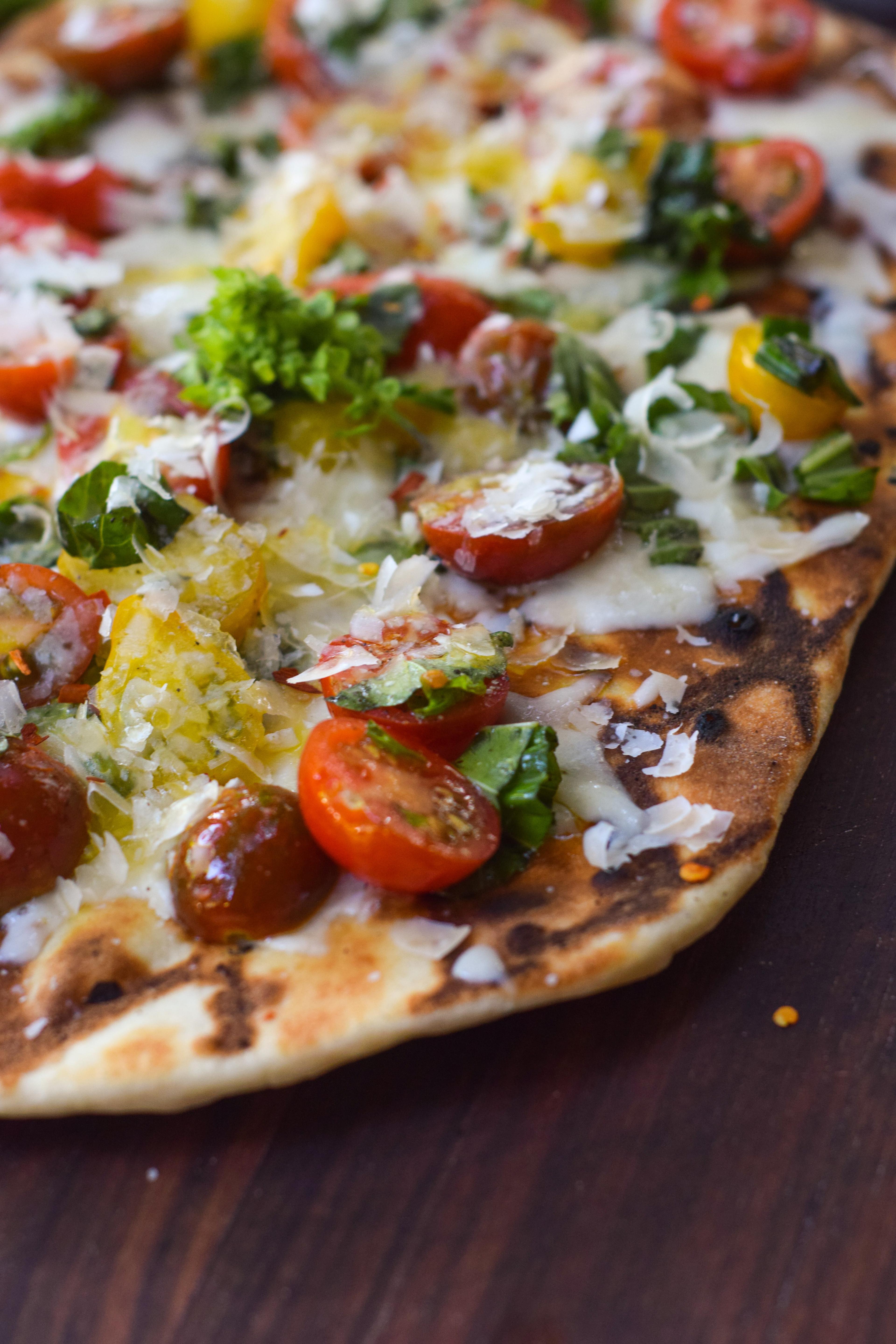 hand arranging grilled tomato and basil flatbread on a plate