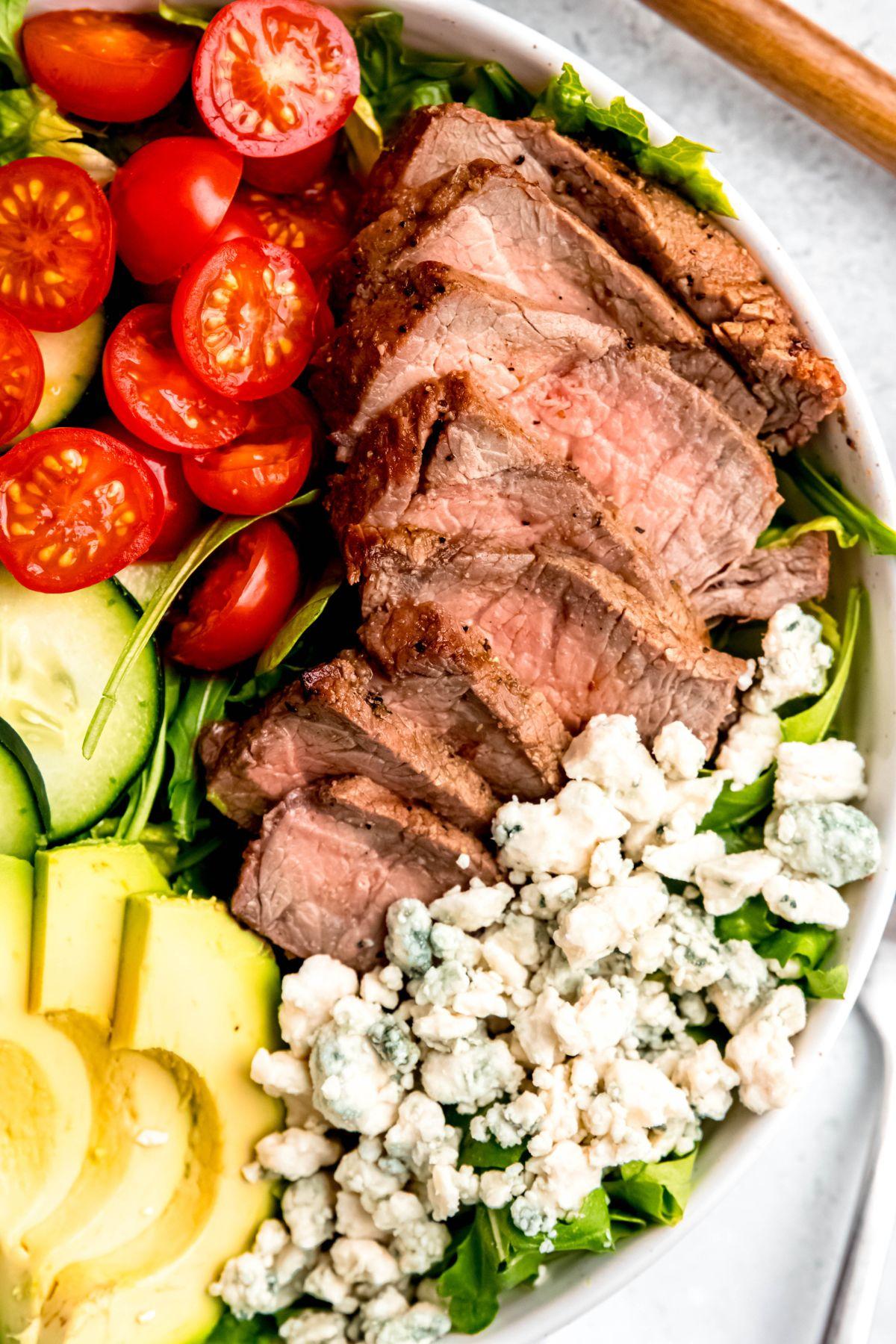 close-up of grilled steak slices on top of a colorful salad with goat cheese