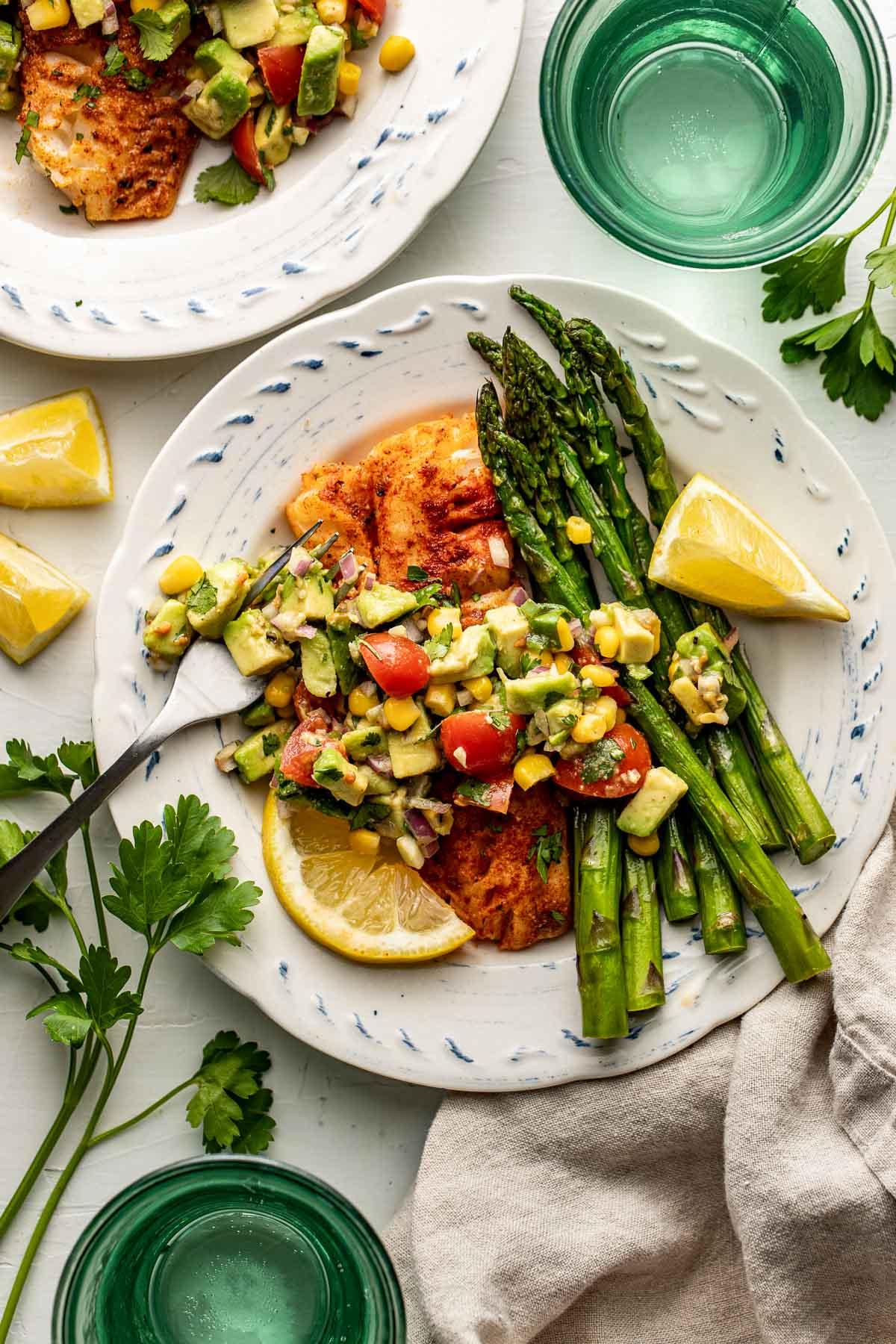 Overhead view of grilled cod topped with roasted red pepper sauce, plated with asparagus and lemon wedges