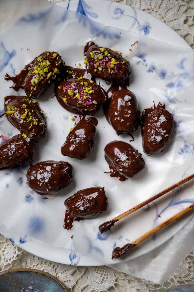 a plate of beautifully arranged chocolate-covered dates, some sprinkled with sea salt and others with chopped nuts