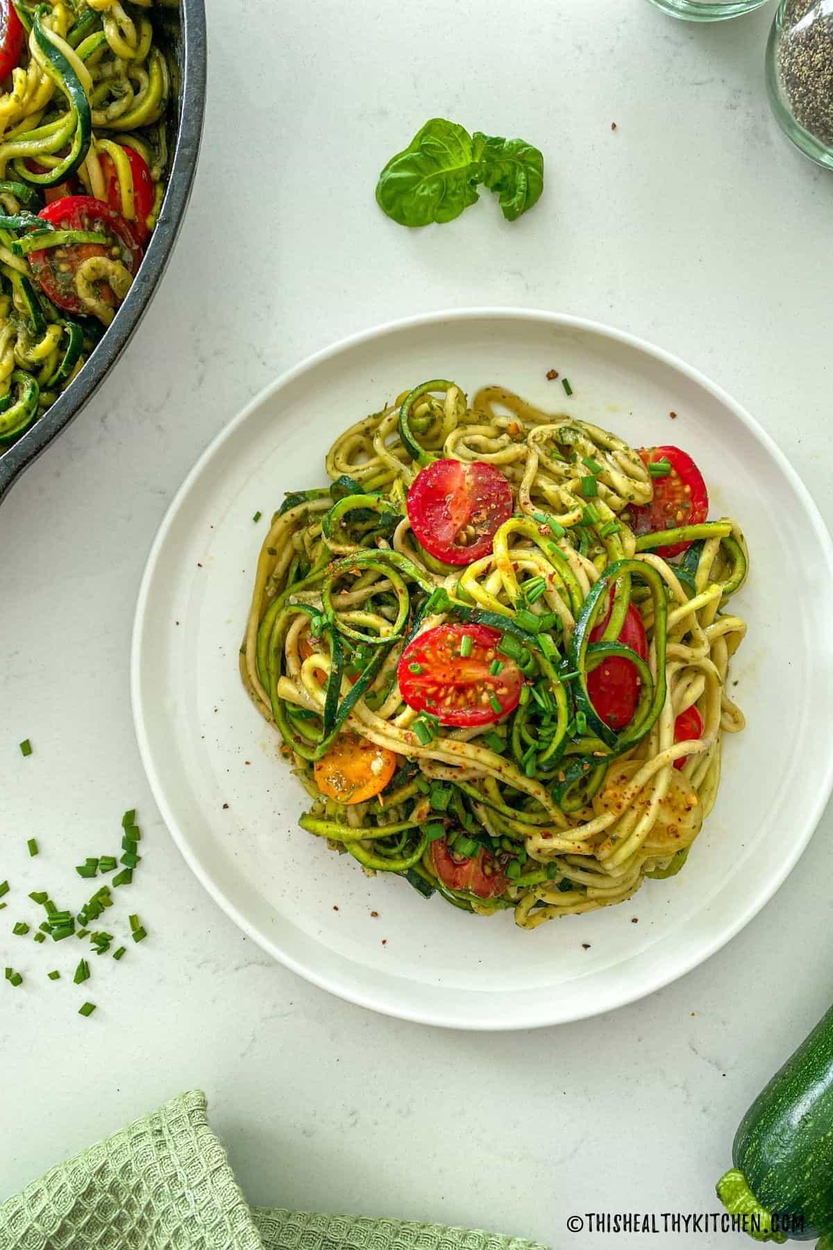 plate of zucchini noodles with pesto and cherry tomatoes garnished with basil