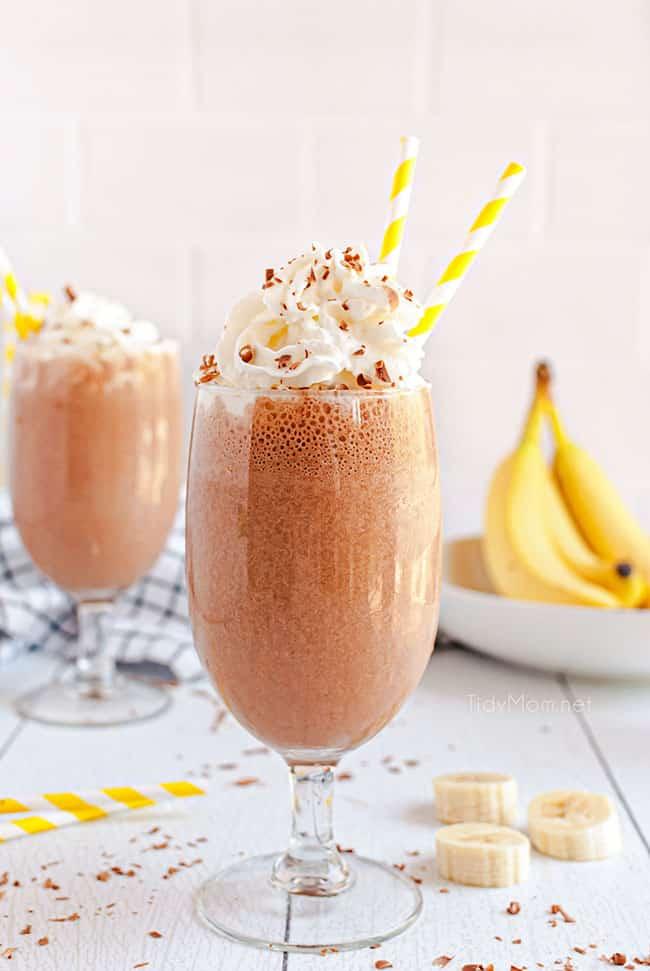 A glass filled with Banana Nutella Milkshake, topped with whipped cream and chocolate shavings