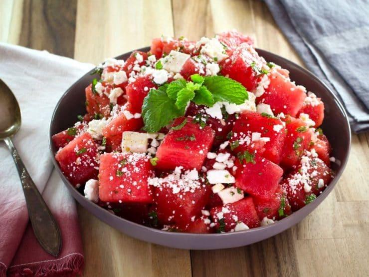 Overhead shot of a Watermelon Feta Salad with Mint on a rustic wooden table, surrounded by fresh ingredients like watermelon, feta, and mint