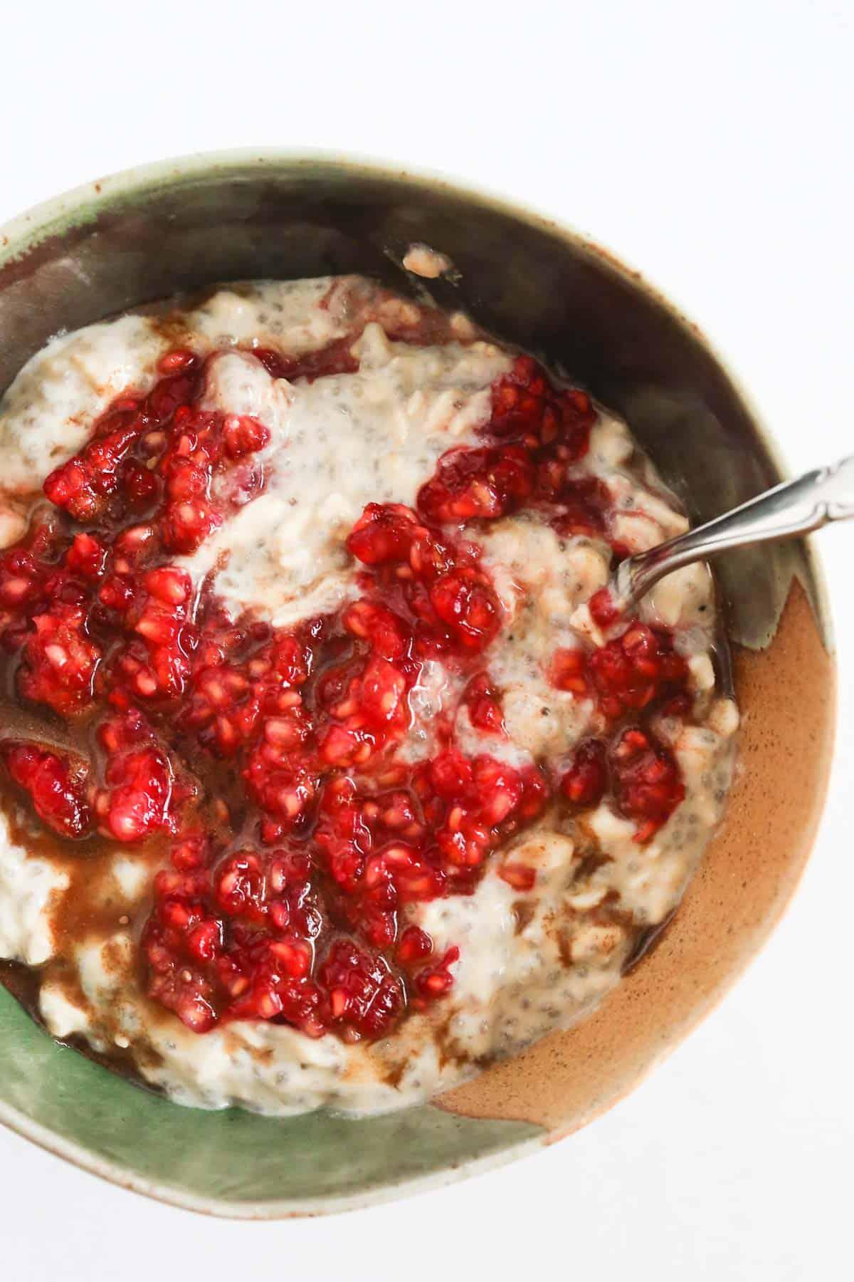 Close-up of a spoon scooping raspberry compote over oats in a bowl