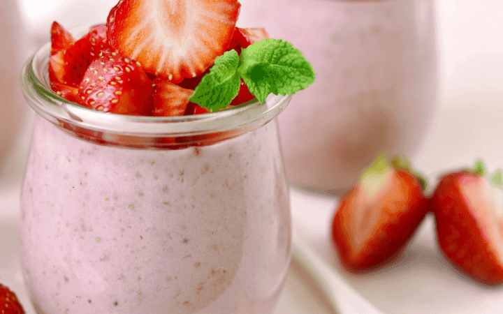 a layered strawberry mousse dessert in a glass, garnished with fresh strawberries and mint