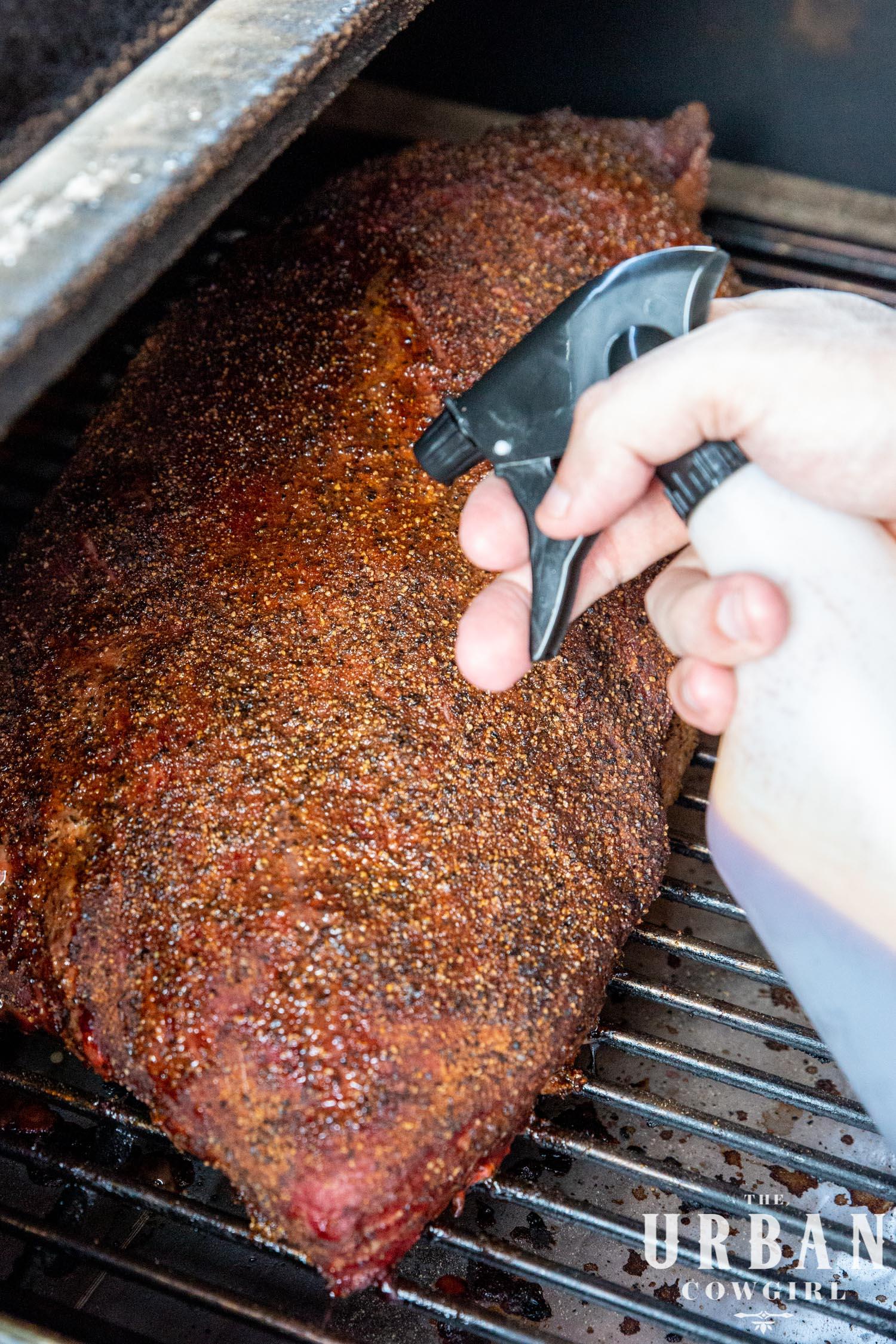 Chef basting a brisket with sauce in a smoker