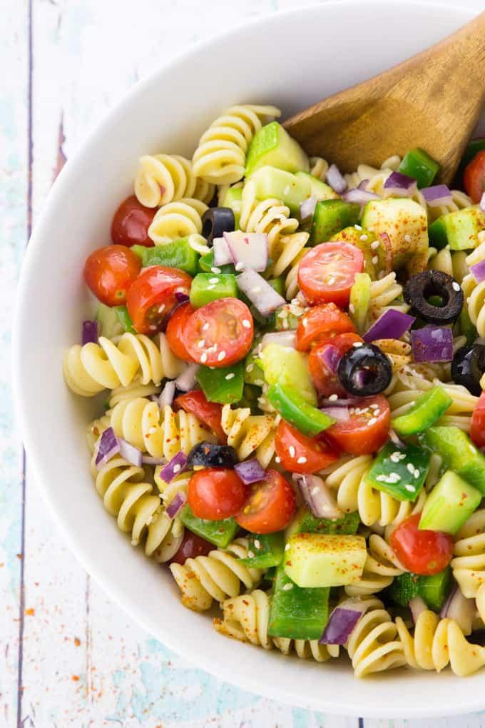a person serving a bowl of california veggie pasta salad