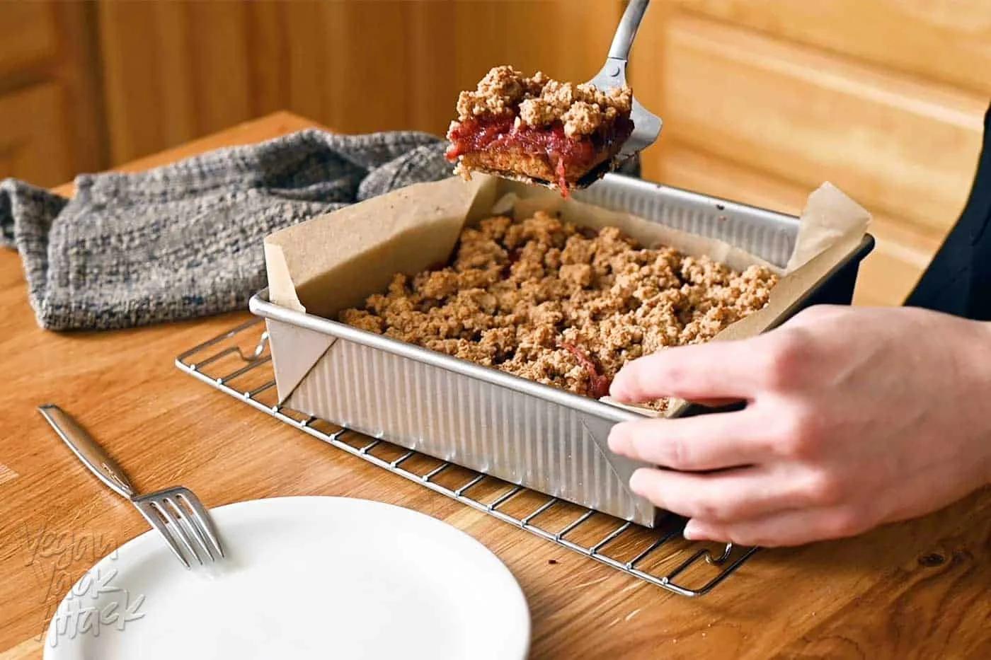 close-up shot of a freshly baked rhubarb crumb bar being lifted from a pan