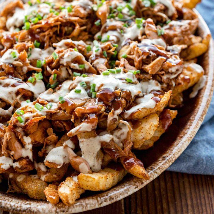 close up shot of loaded fries being drizzled with bbq ranch dressing